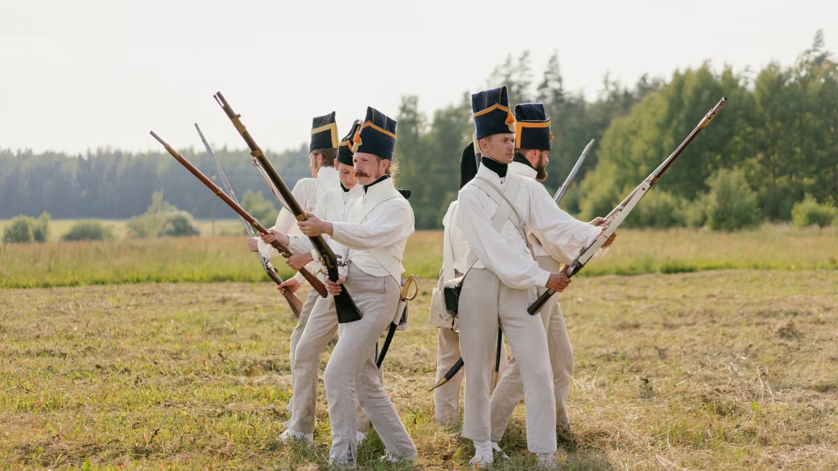 Men in vintage military uniforms recreate historic battle scenes outdoors.